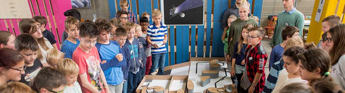 Kinder stehen um einen Tisch und schauen einem Projekt zu