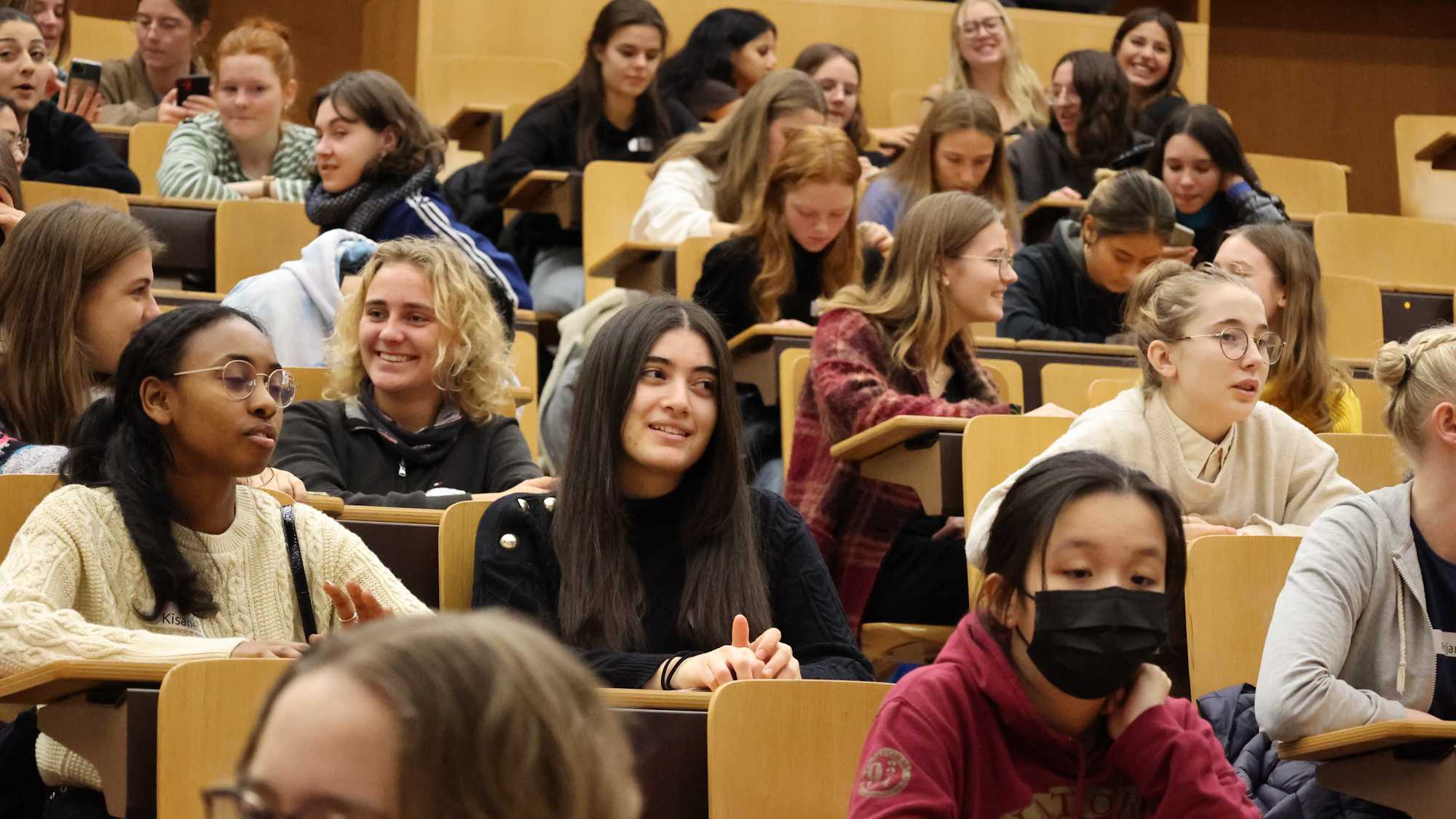 Numerous high school girls sit in the lecture hall and chat