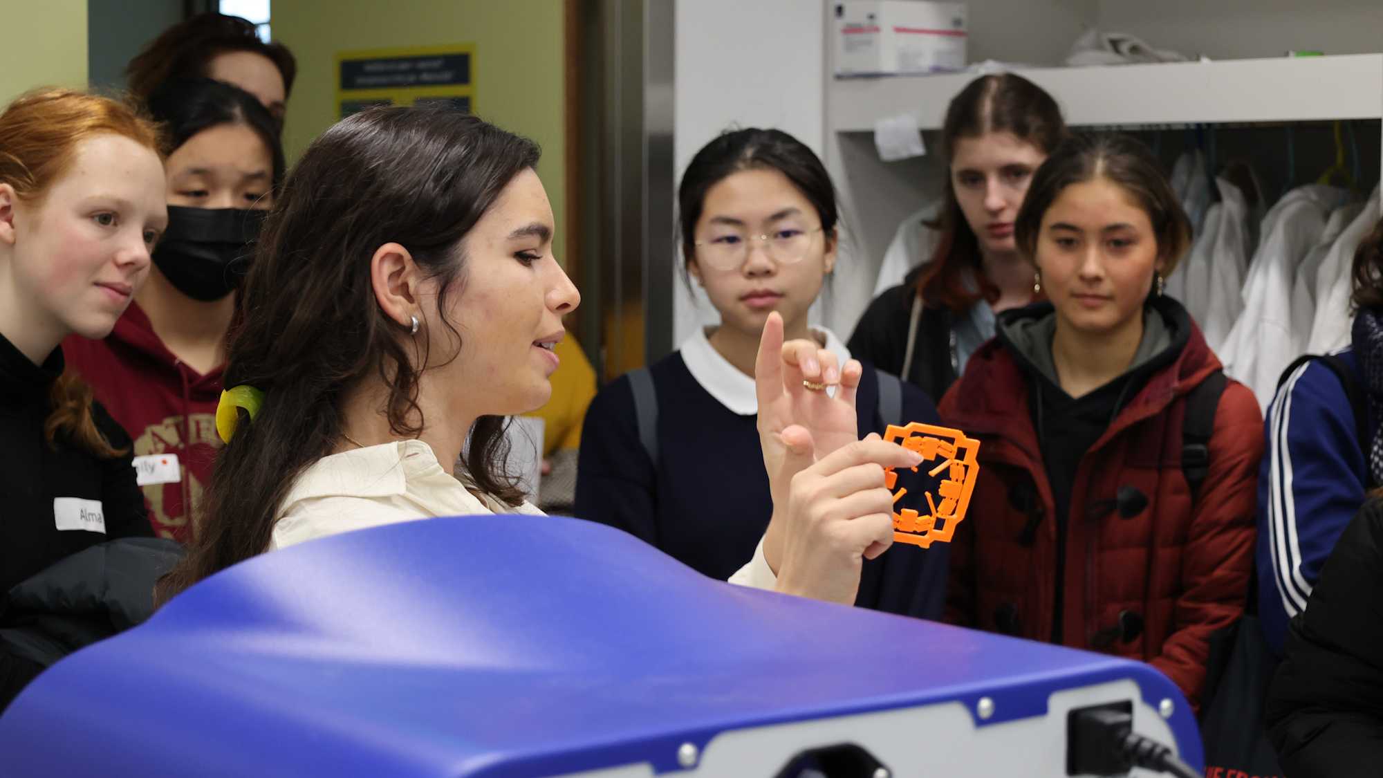 Female high school students look with interest at an object shown by a researcher