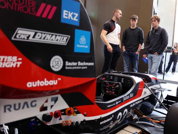 Enlarged view: Racing car in the foreground, behind it three visitors in conversation